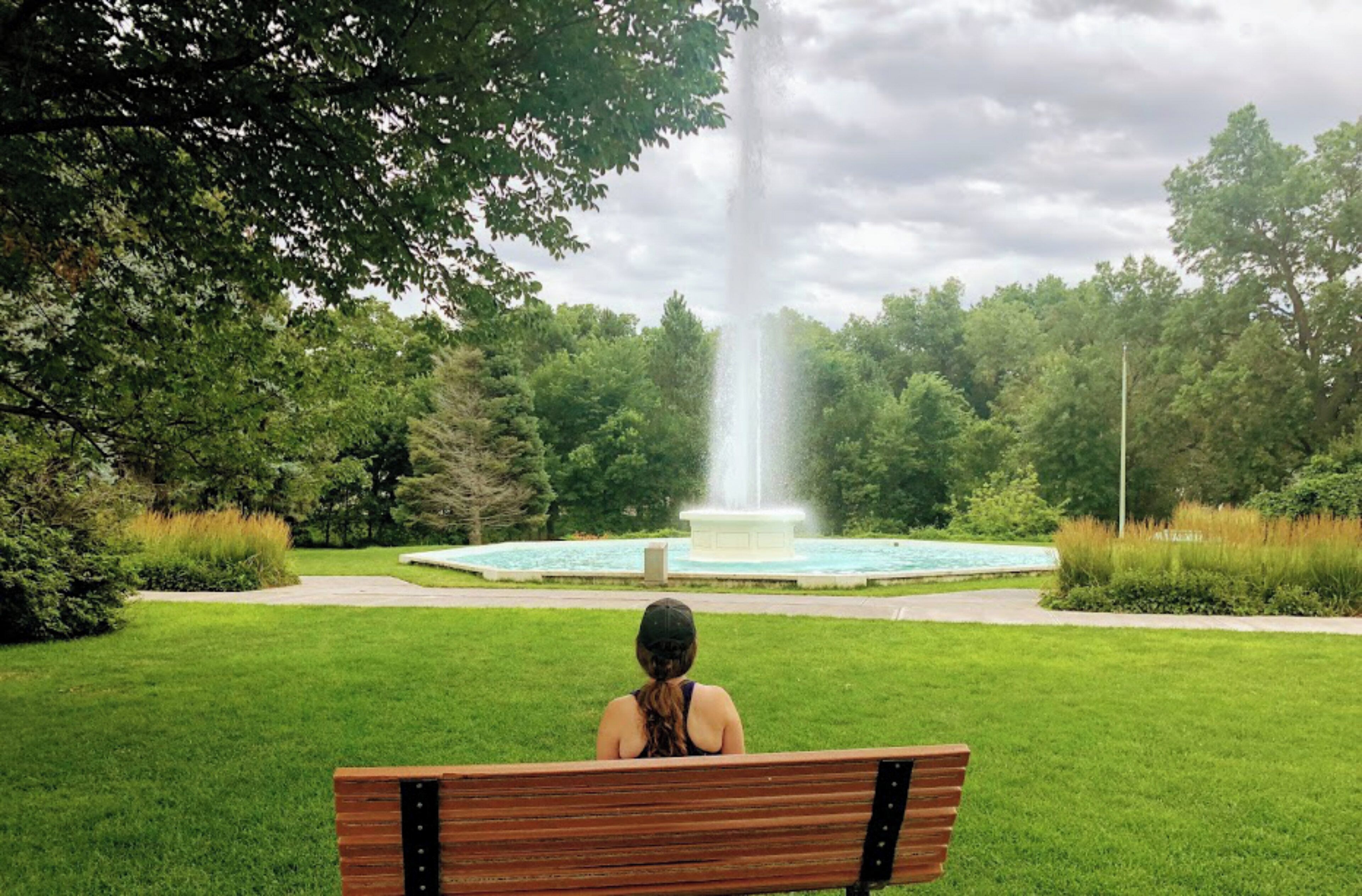 Un parque con una fuente, un banco y un césped bien cuidado.