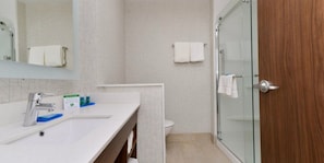 A modern bathroom with a white sink, a glass shower enclosure, and a wooden door. - Holiday Inn Express Alliance by IHG (Alliance)