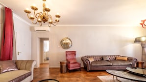 A living room with a brown leather sofa, a red armchair, a glass coffee table, and a chandelier. - Casa Verona (Venice)