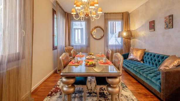 A dining area with a table set for four, surrounded by chairs, a chandelier, and a sofa. - Casa Verona (Venice)
