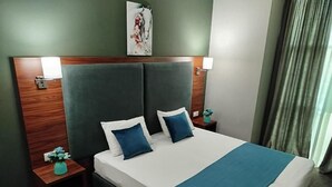 A neatly made bed with a blue accent, a wooden headboard, and two bedside tables with lamps. - Green Tower Hotel (Tbilisi)
