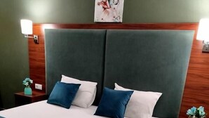A neatly made bed with a blue and white bedspread, two blue pillows, and a wooden headboard. There are two bedside tables with decorative vases on them. - Green Tower Hotel (Tbilisi)
