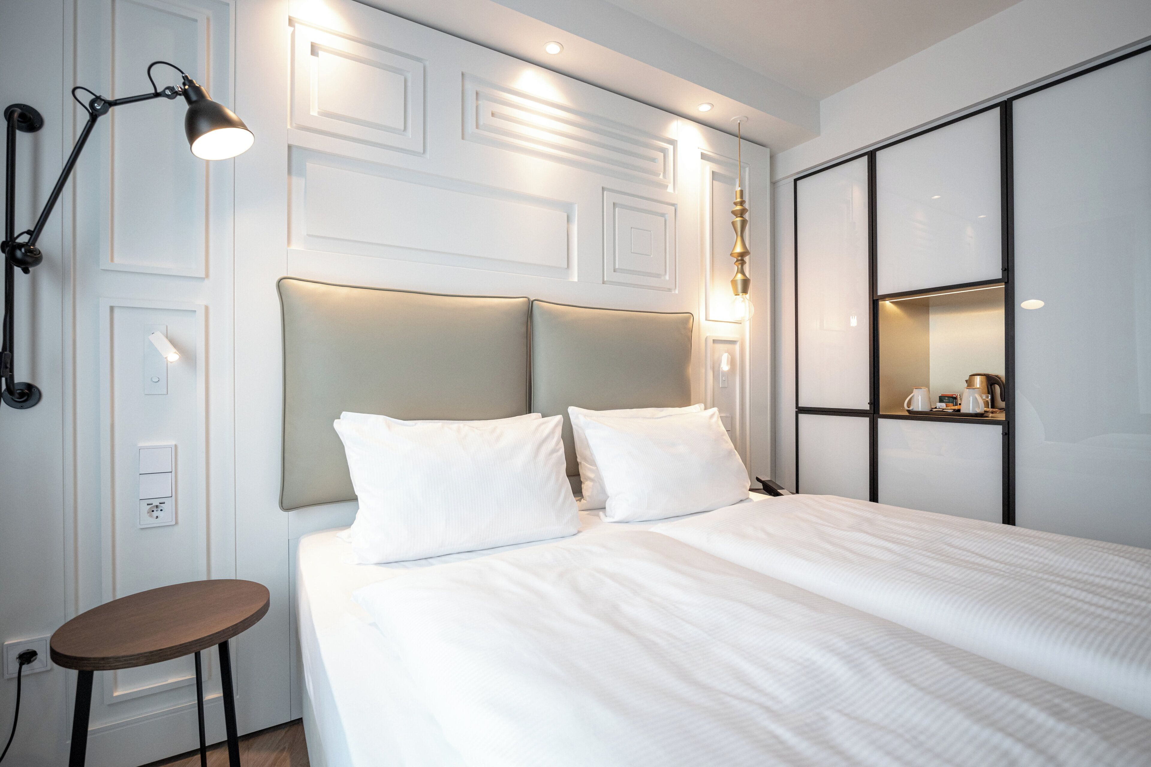 A neatly arranged hotel room with a bed, bedside lamp, and a small table.
