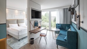 A modern hotel room with a bed, a sofa, a small table, and a TV mounted on the wall.