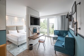 Una habitación de hotel moderna con una cama, un sofá, una mesita y un televisor montado en la pared.