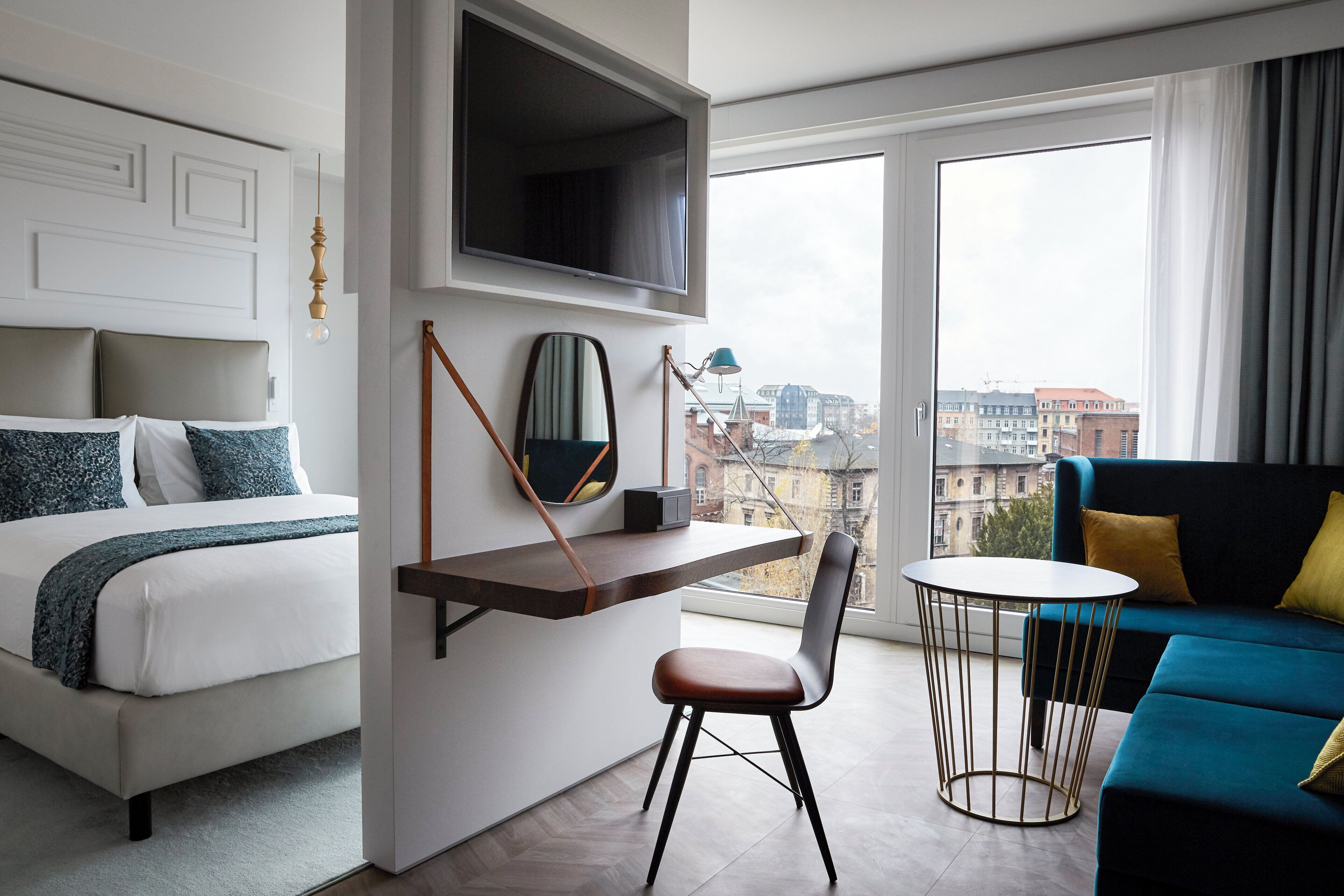 A hotel room with a bed, a desk, a chair, a sofa, and a TV mounted on the wall.