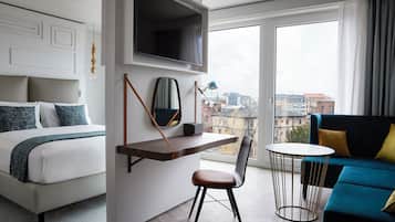 A hotel room with a bed, a desk, a chair, a sofa, and a TV mounted on the wall.