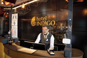 A hotel reception desk with a digital screen, a guest card reader, and a sign for hotel Indigo. - Hotel Indigo Dresden - Wettiner Platz by IHG (Dresden)