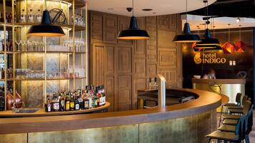 A bar area with a curved counter, shelves with bottles, glasses, and a sign for 'hotel INDIGO'.