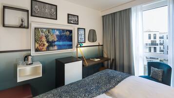 Habitación de hotel con cama, escritorio, silla y una ventana grande con vista a edificios.