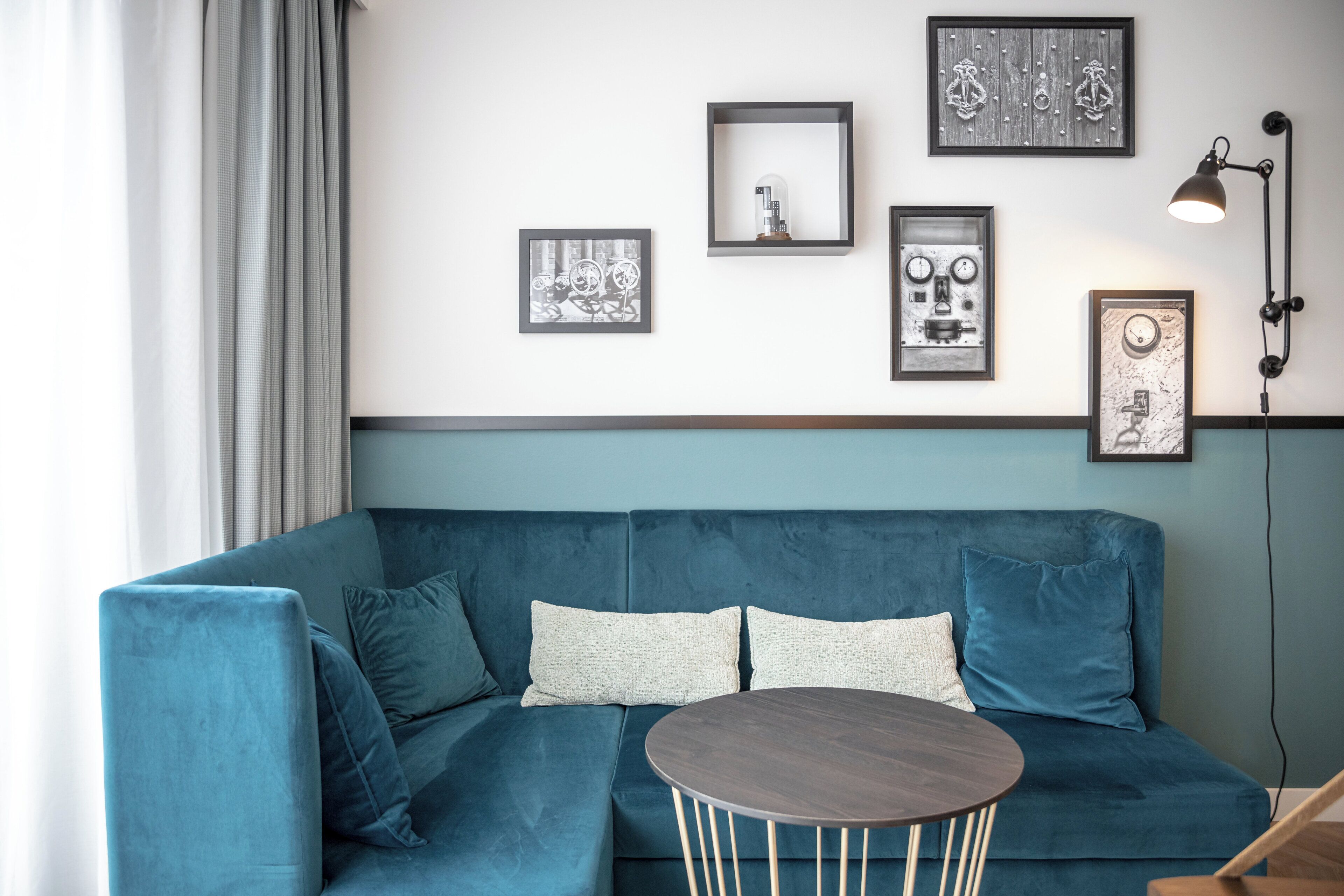 Ein modernes Wohnzimmer mit einem türkisfarbenen Sofa, einem runden Couchtisch und mehreren gerahmten Kunstwerken an der Wand.