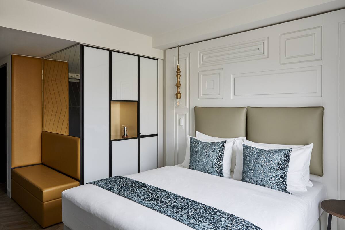 A modern hotel room with a large bed, a seating area, and a wardrobe.
