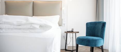 Een hotelkamer met een bed, een stoel, een nachtkastje en een wandlamp.