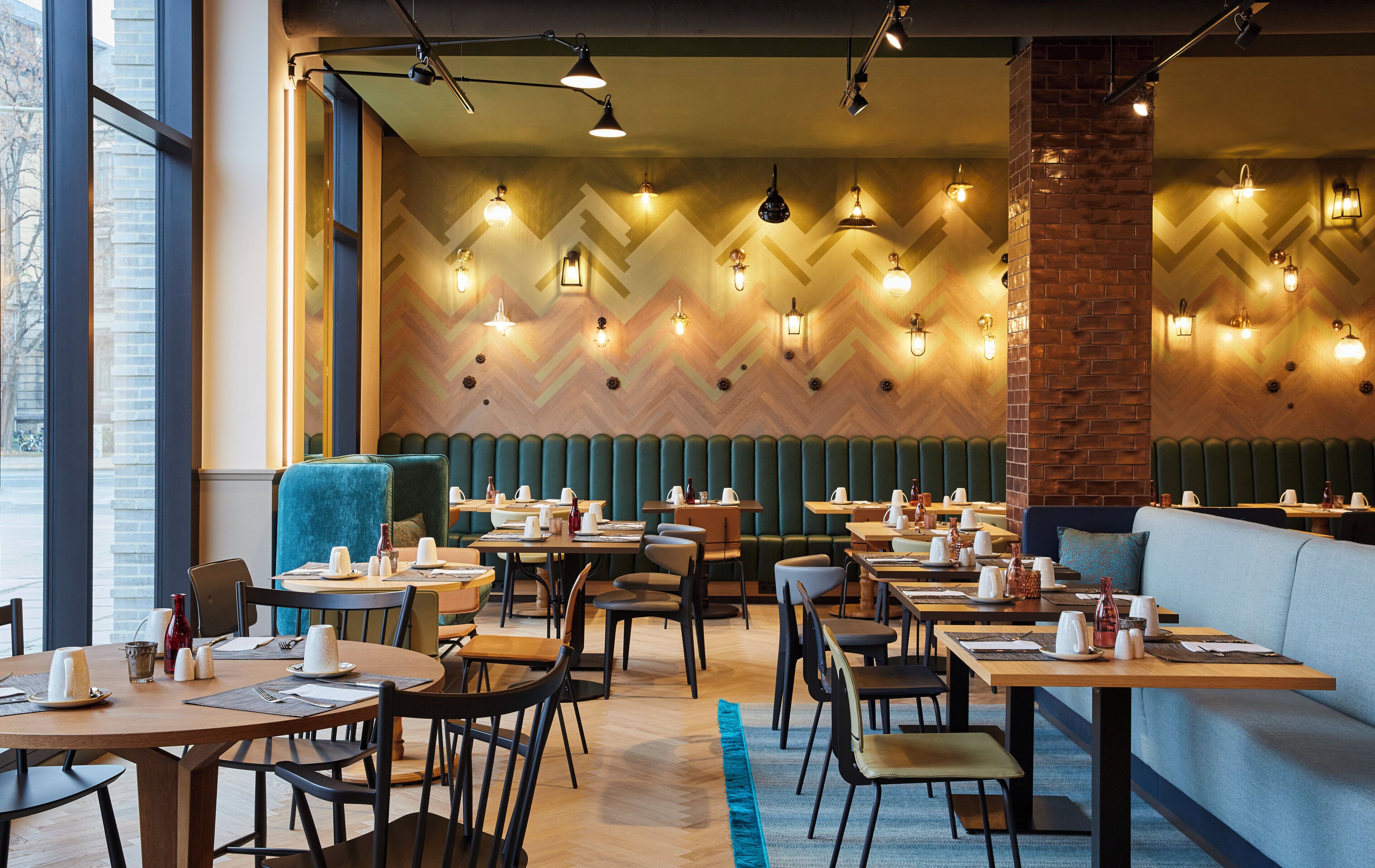 Interior de restaurante com várias mesas, cabines e uma parede de tijolos decorativa.
