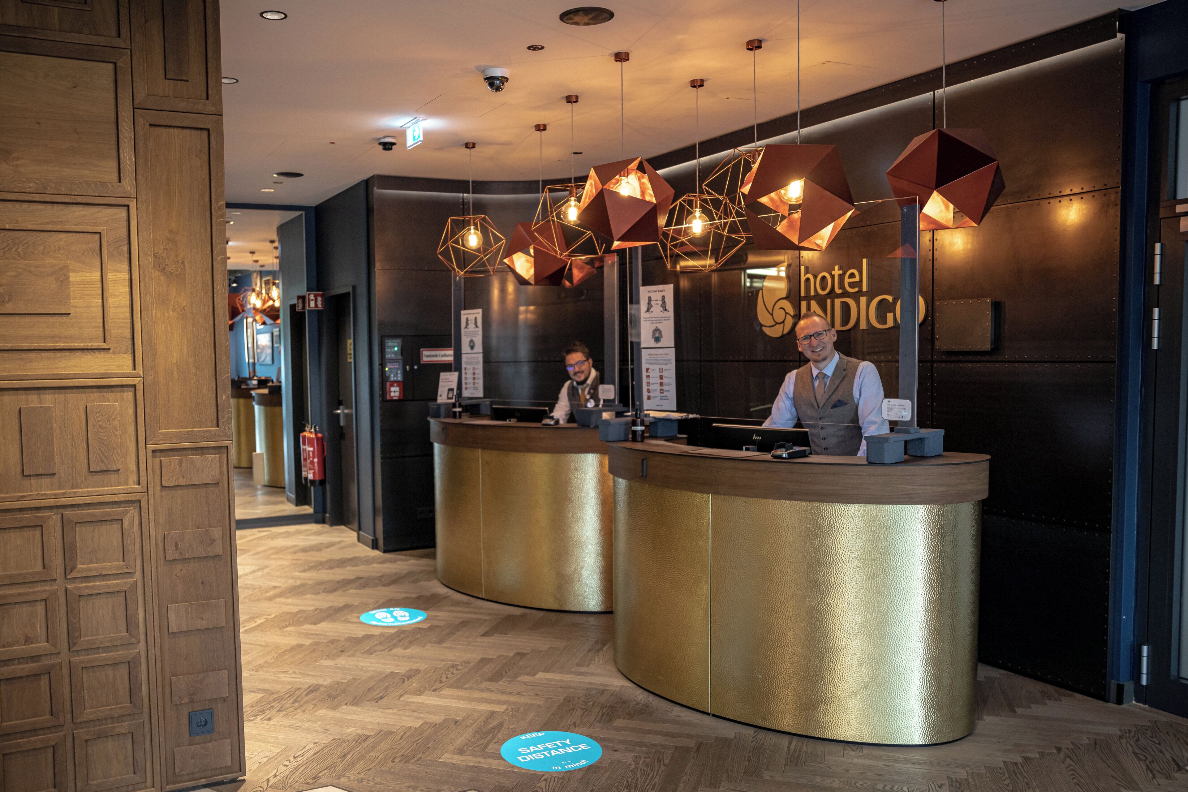 A hotel reception desk with a modern design, a receptionist, and a sign indicating the hotel name.