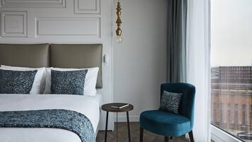Habitación de hotel con cama, una silla, una mesita y ventana con vista a la ciudad.