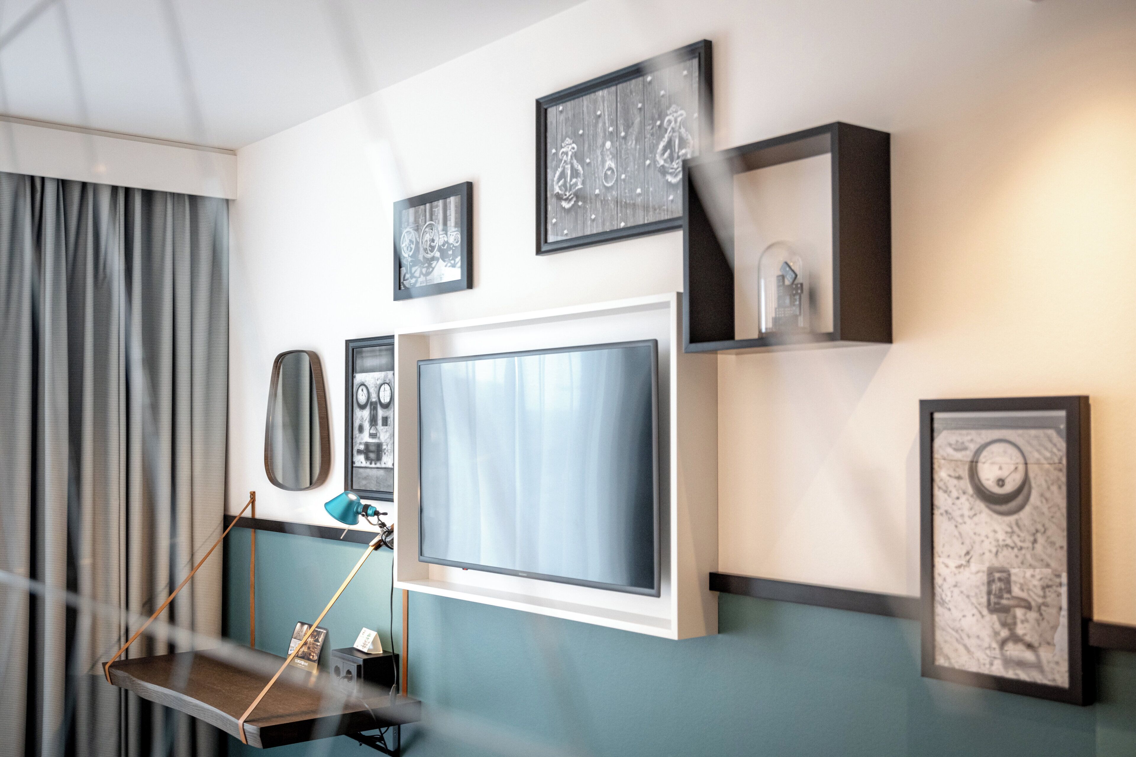 A modern room with a large flat-screen TV, a desk with a lamp, and various framed pictures on the wall.