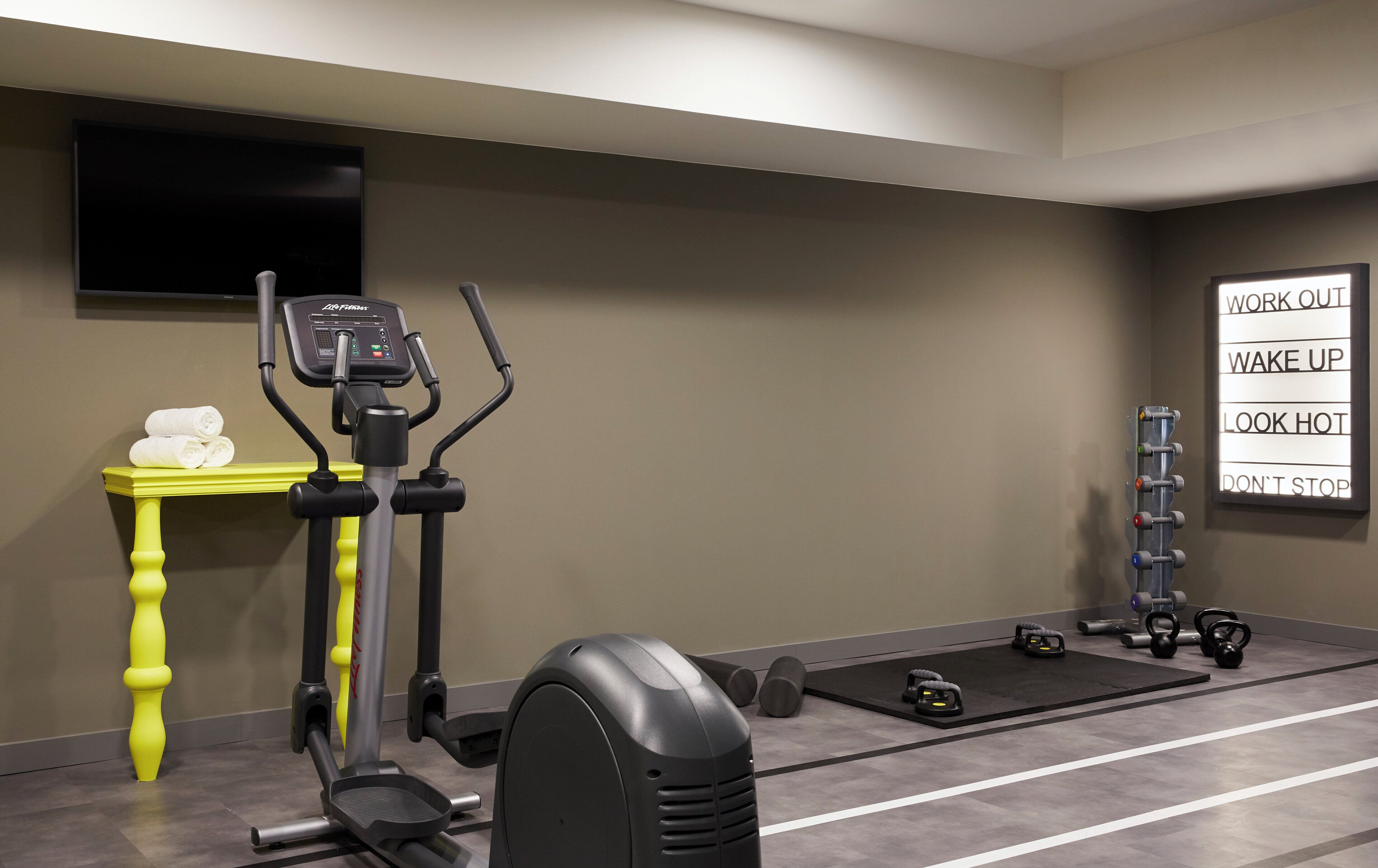 Ein Fitnessraum mit Trainingsgeräten, einem Fernseher und motivierenden Postern an der Wand.