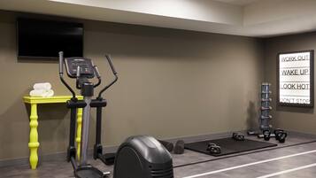 Ein Fitnessraum mit Trainingsgeräten, einem Fernseher und motivierenden Postern an der Wand.