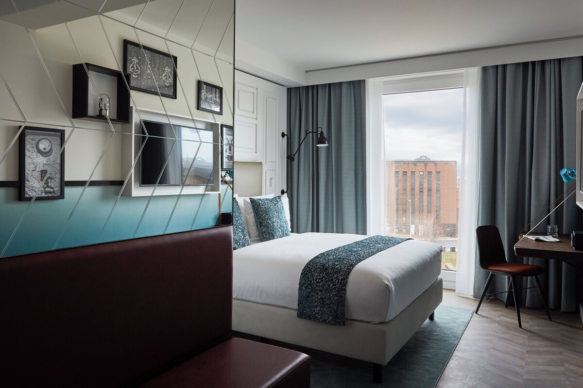 Una habitación de hotel moderna con una cama grande, un escritorio, una silla y vistas a la ciudad.