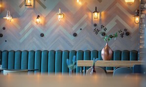 A modern interior with a chevron-patterned wall, cushioned seating, and a wooden table with a vase of flowers. - Hotel Indigo Dresden - Wettiner Platz by IHG (Dresden)