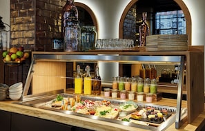 A buffet with a variety of food items, including fruits, cheeses, and meats, as well as a selection of beverages in bottles and glasses. - Hotel Indigo Dresden - Wettiner Platz by IHG (Dresden)