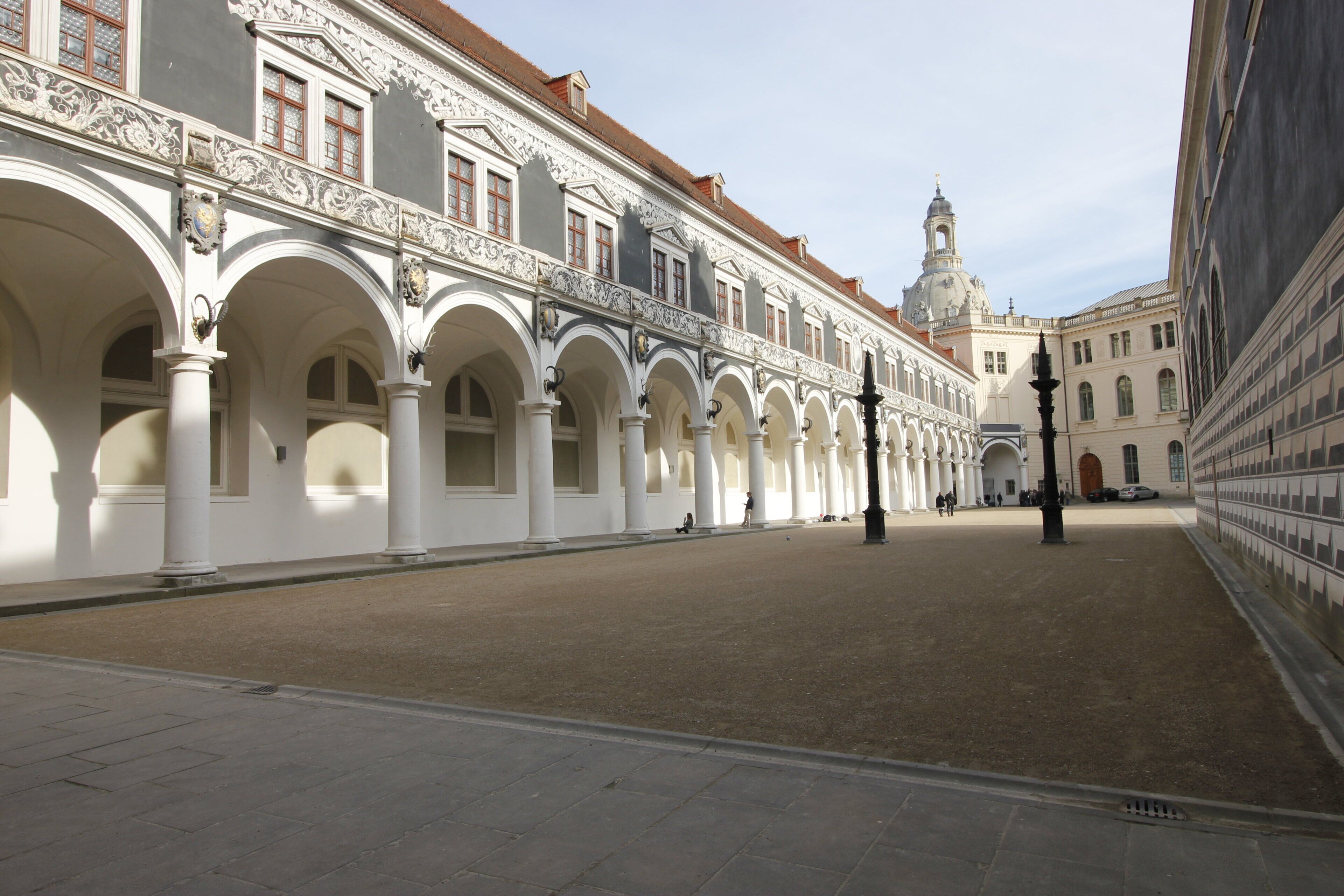 A courtyard with white columns and arches, a fountain, and a building with a dome in the background.