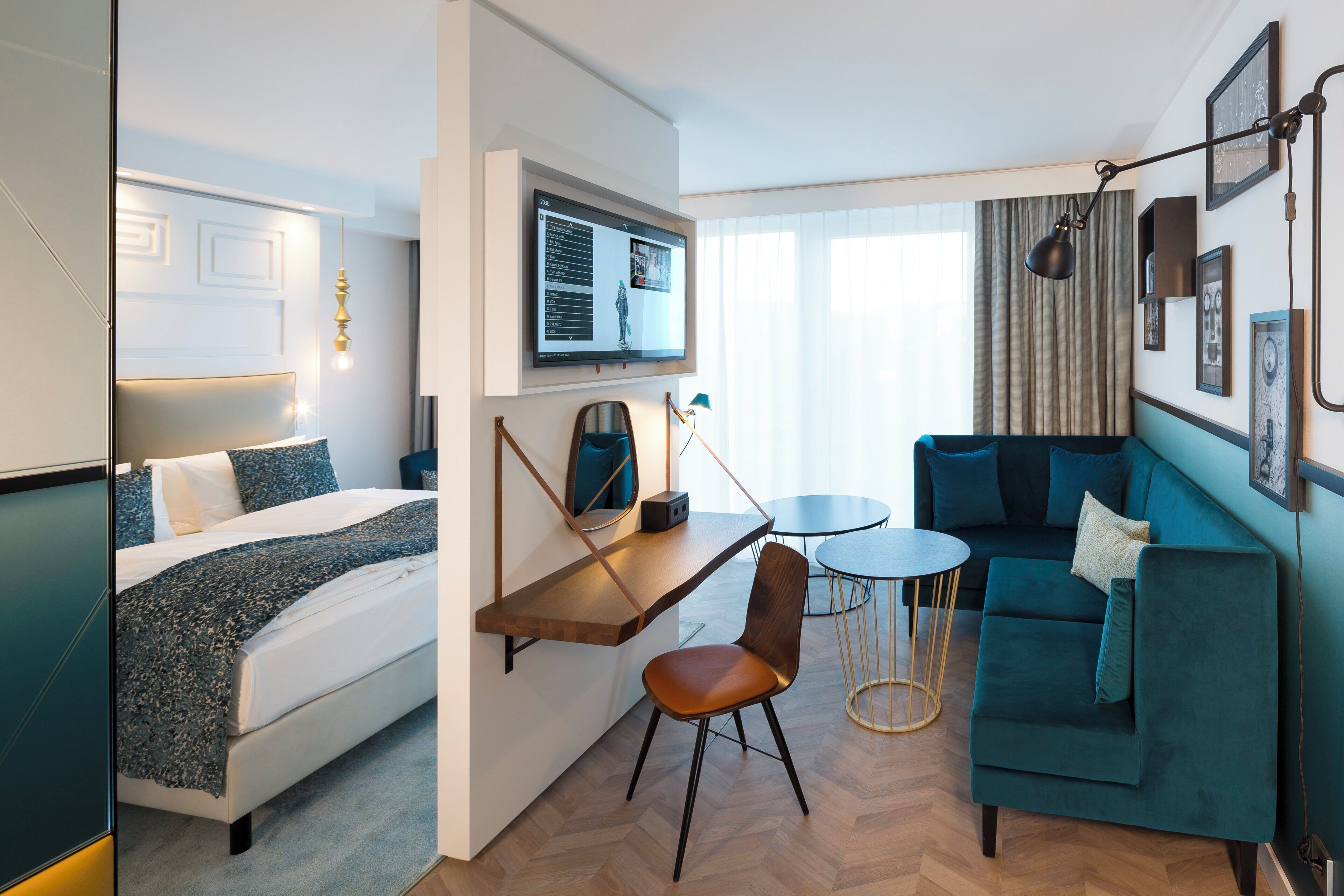 A modern hotel room with a bed, a desk, a sofa, and a TV.