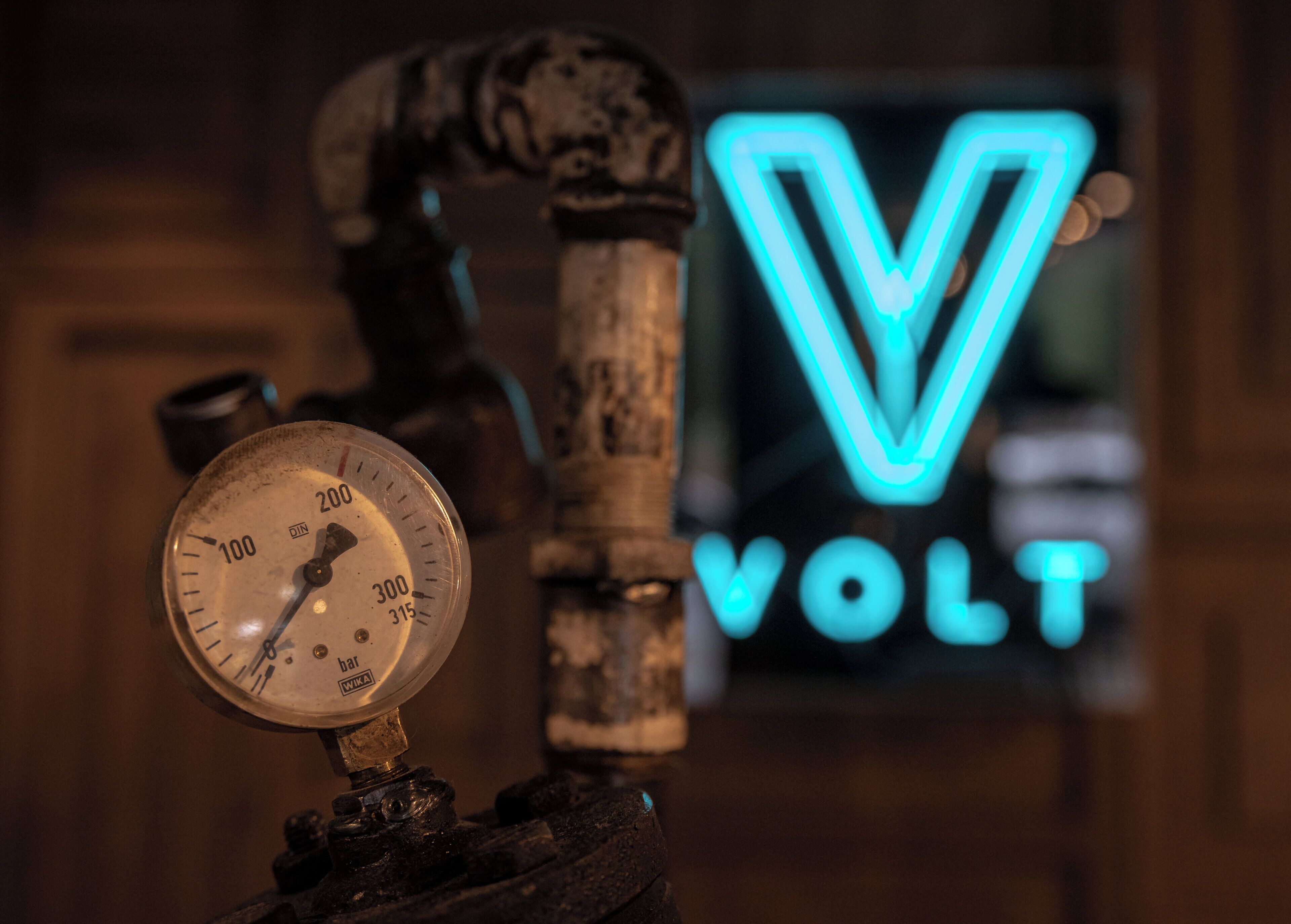 A gauge and a neon sign with the word 'VOLT' in the background.