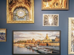 Un mur orné de plusieurs œuvres d’art encadrées, dont une horloge, une vue de ville et une photographie en noir et blanc.