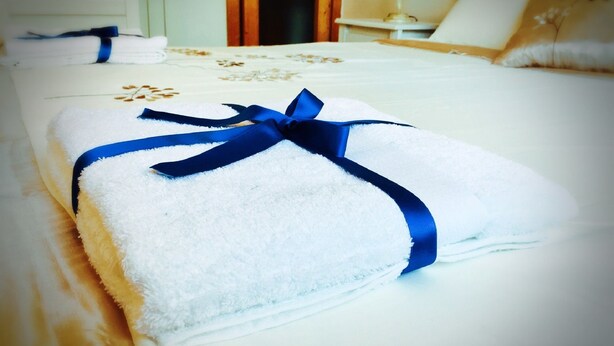 A neatly made bed with a blue ribbon, a white wall with a picture frame, and a wooden door in the background. - Aloha House (Formia)