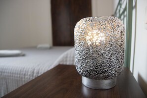 A metallic, intricately designed lamp on a wooden table in a room with a bed in the background. - Aloha House (Formia)