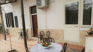 A patio with a round table and chairs, a flower vase, and a door with a window. - Aloha House (Formia)