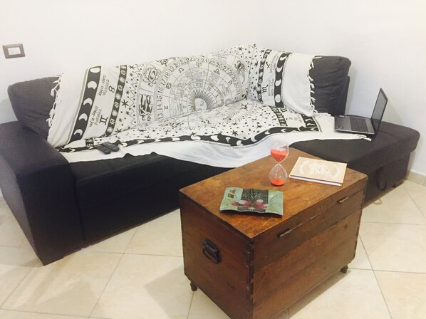 A living room with a black sofa, a wooden coffee table with a book and an hourglass, and a laptop on the sofa.