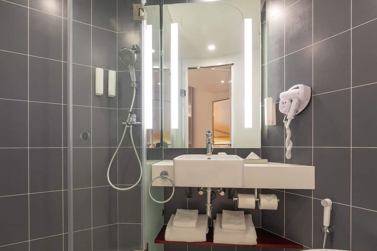 Un baño moderno con ducha de vidrio, un lavamanos blanco y un secador de pelo montado en la pared.