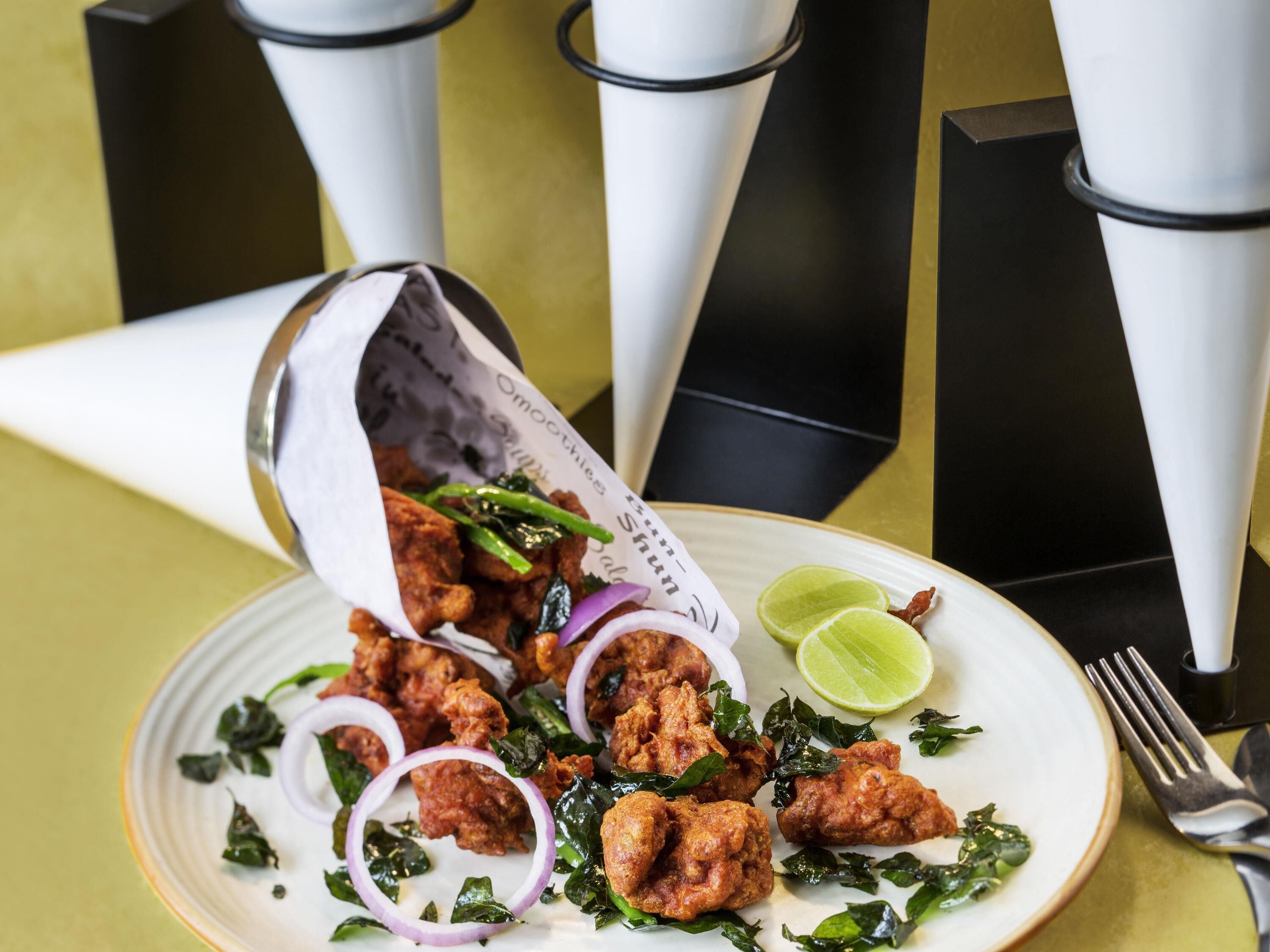 A plate of fried chicken with onions and lime, served on a white plate with a gold rim.