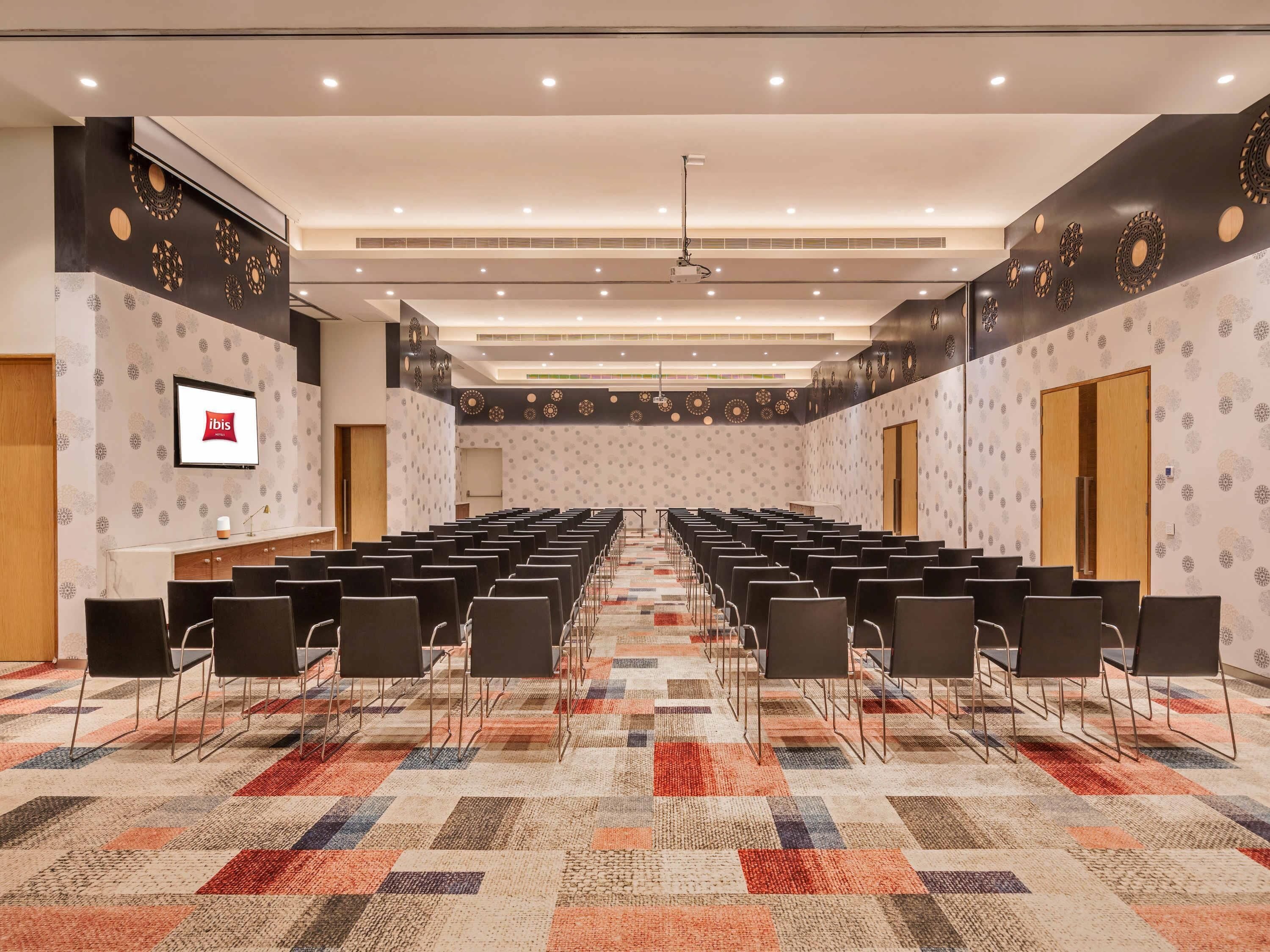 A conference room with rows of chairs, a carpeted floor, and a screen on the wall.