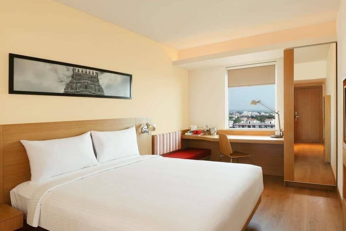 Habitación de hotel con cama, escritorio, silla, ventana con vistas y puerta.