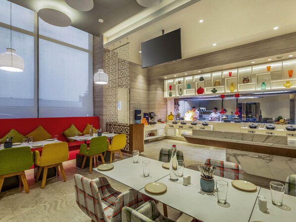Un restaurante moderno con barra central, mesas de comedor con sillas y cocina al fondo.