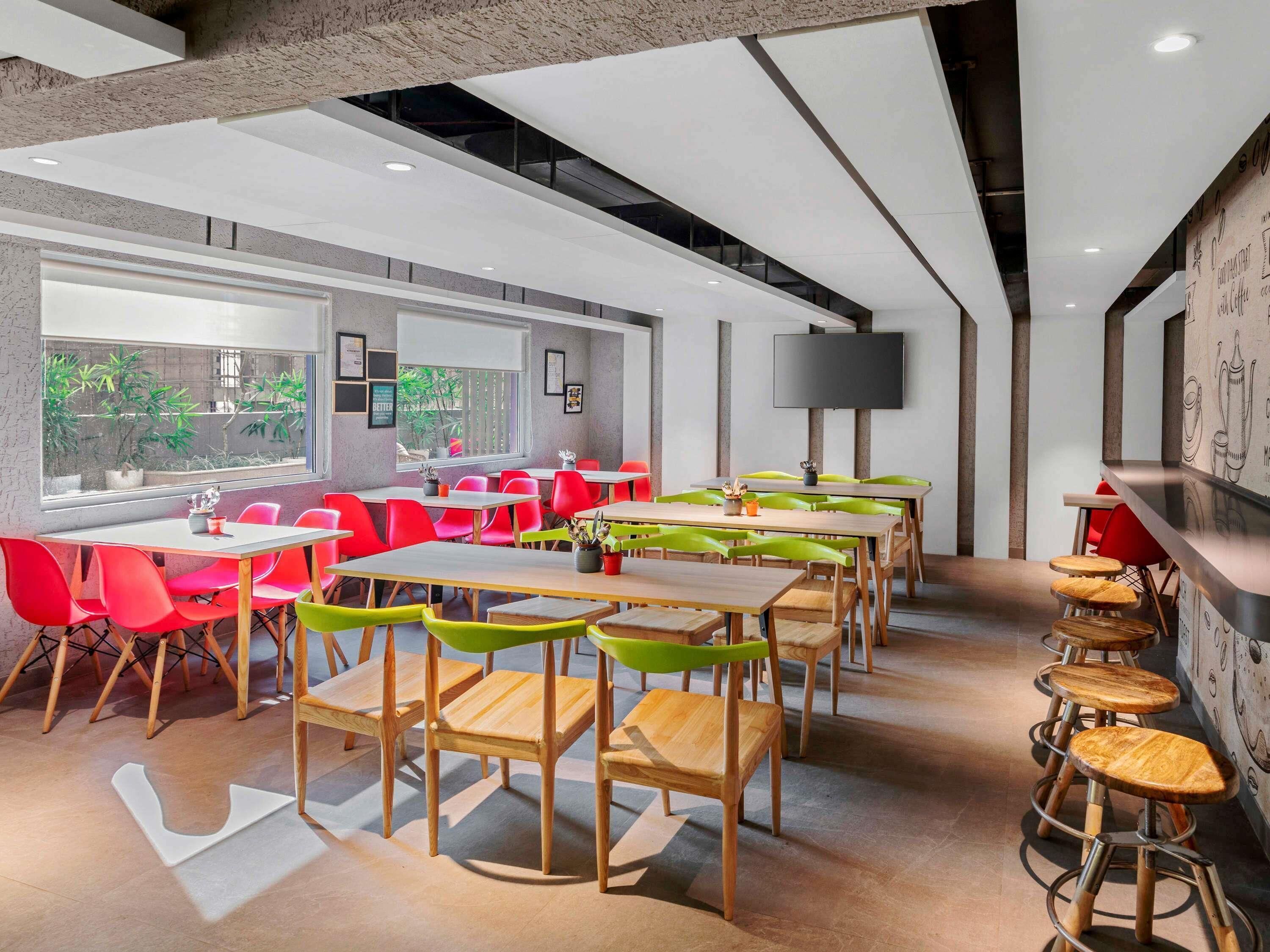 A modern dining area with multiple tables and chairs, a large window with plants, and a bar counter.