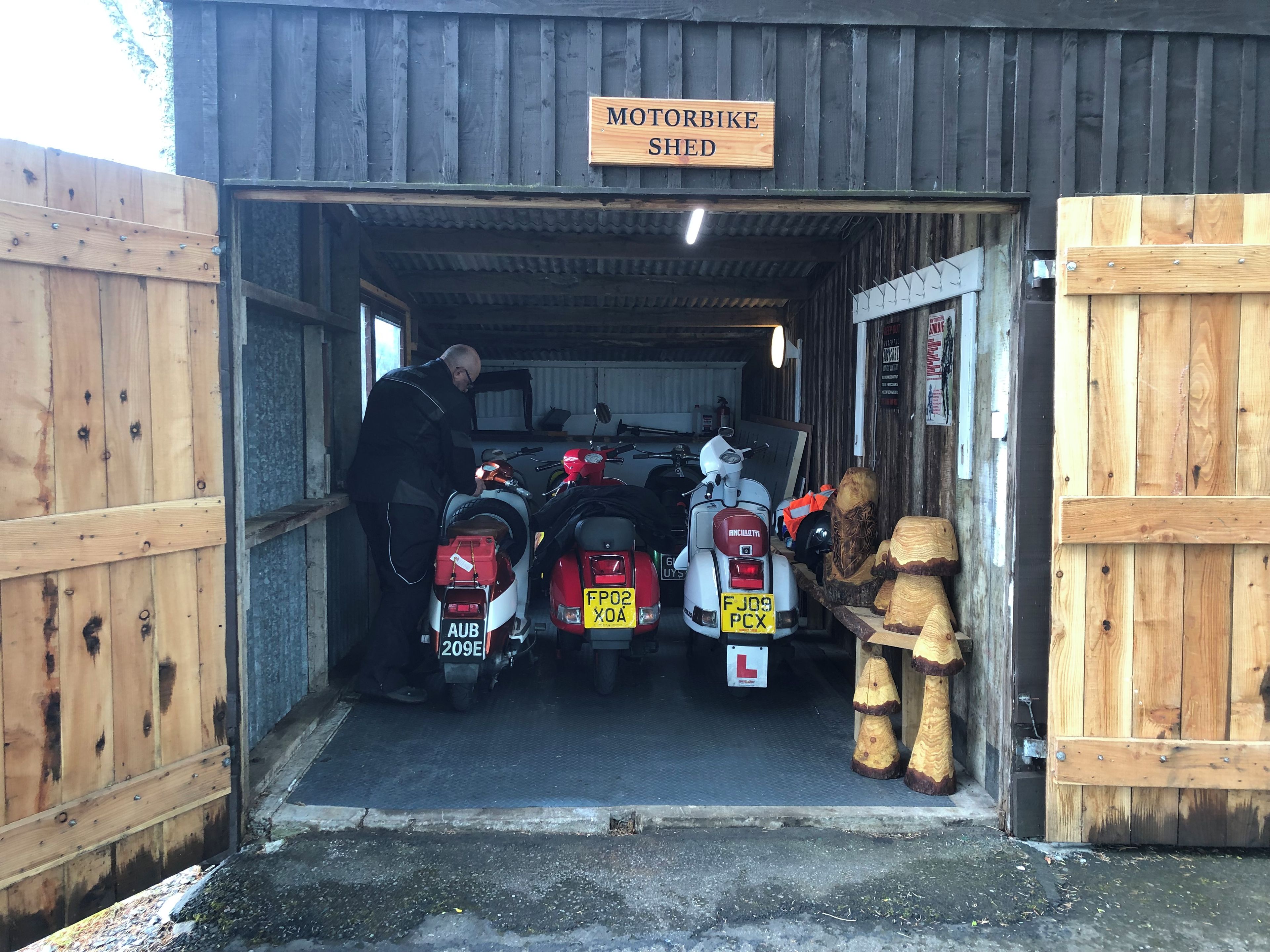A motorbike shed with a sign, a person, and two motorbikes inside.