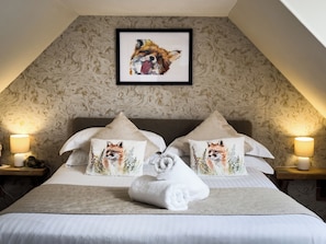A neatly made bed with two pillows featuring fox illustrations, a framed artwork above, and a lamp on each side.