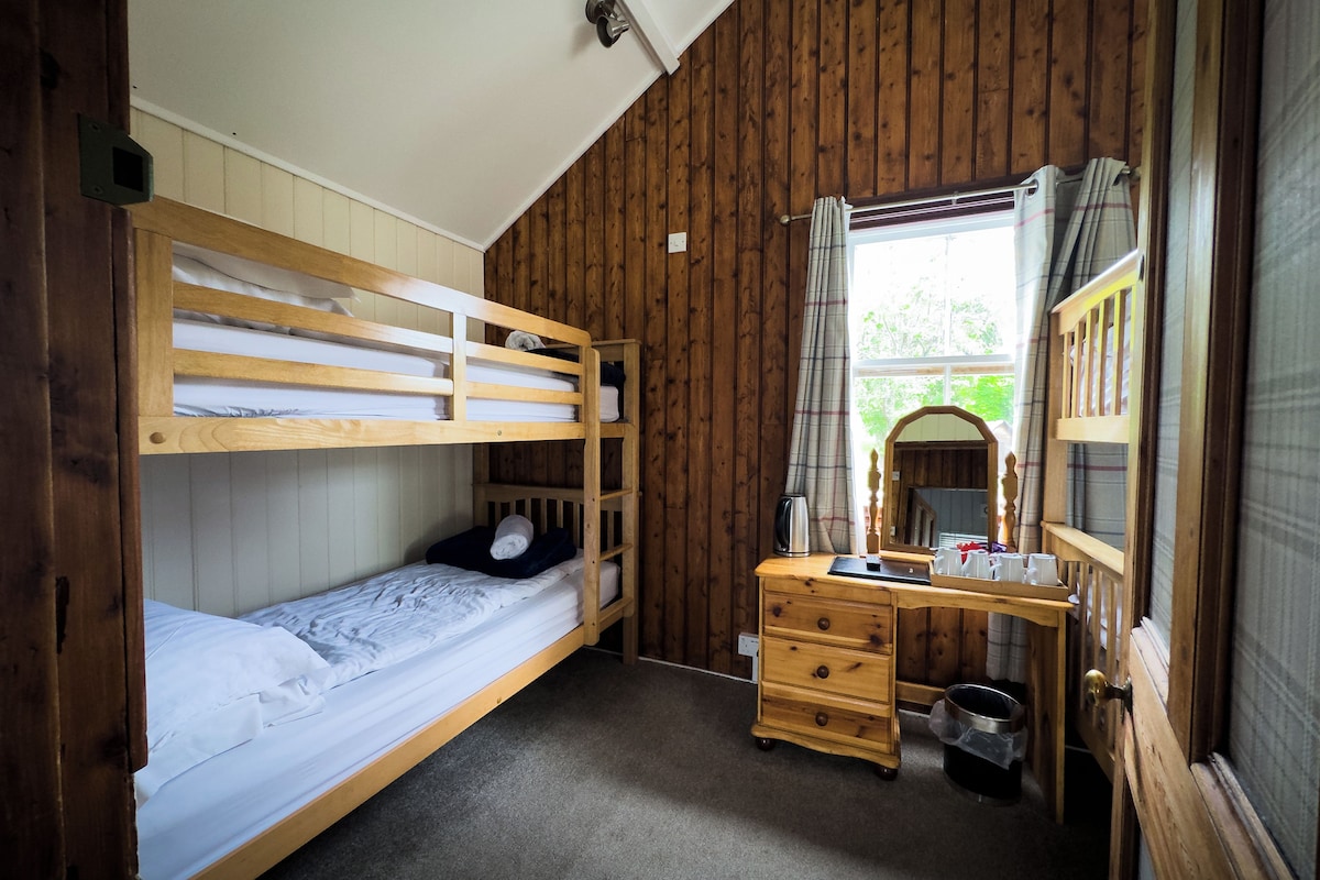 A bunk bed with a desk and a mirror, wooden walls, and a window with curtains.