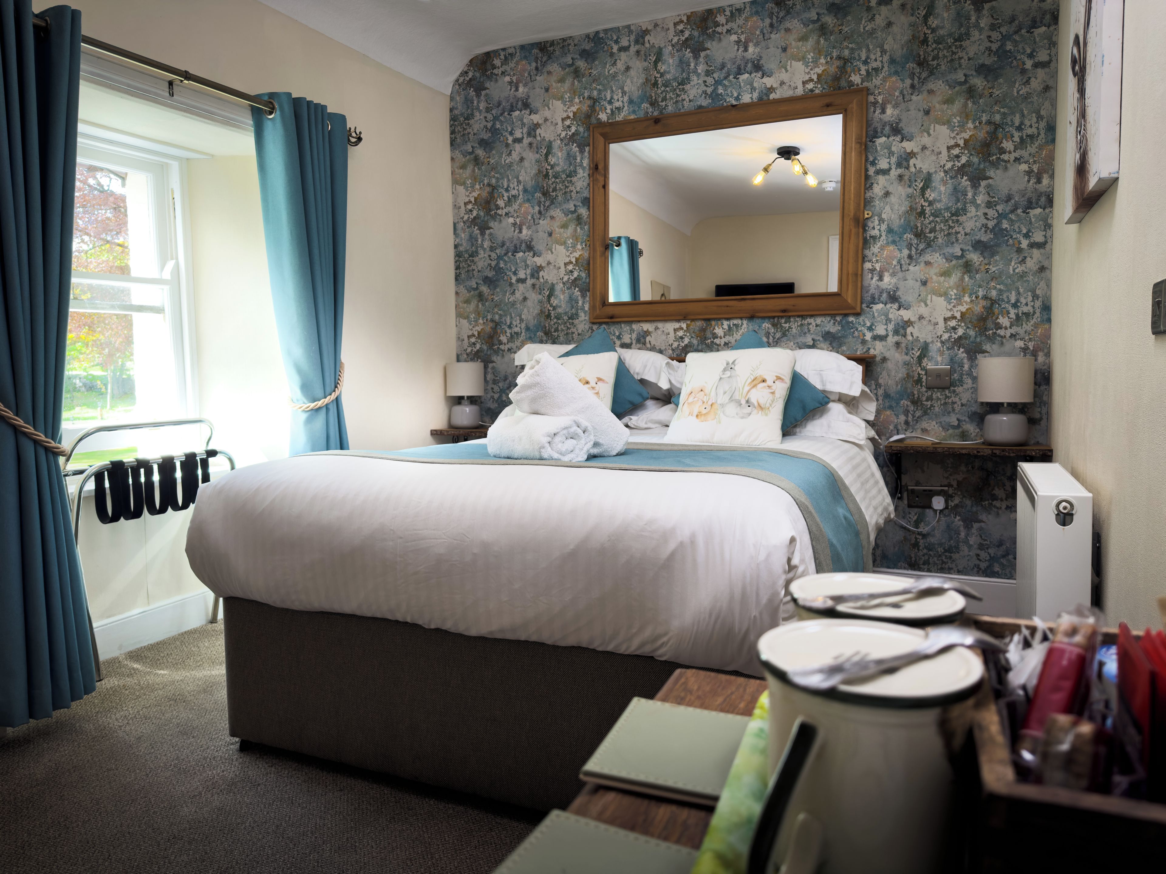 A hotel room with a large bed, a bedside table with a lamp, a mirror, and a view of the outdoors.