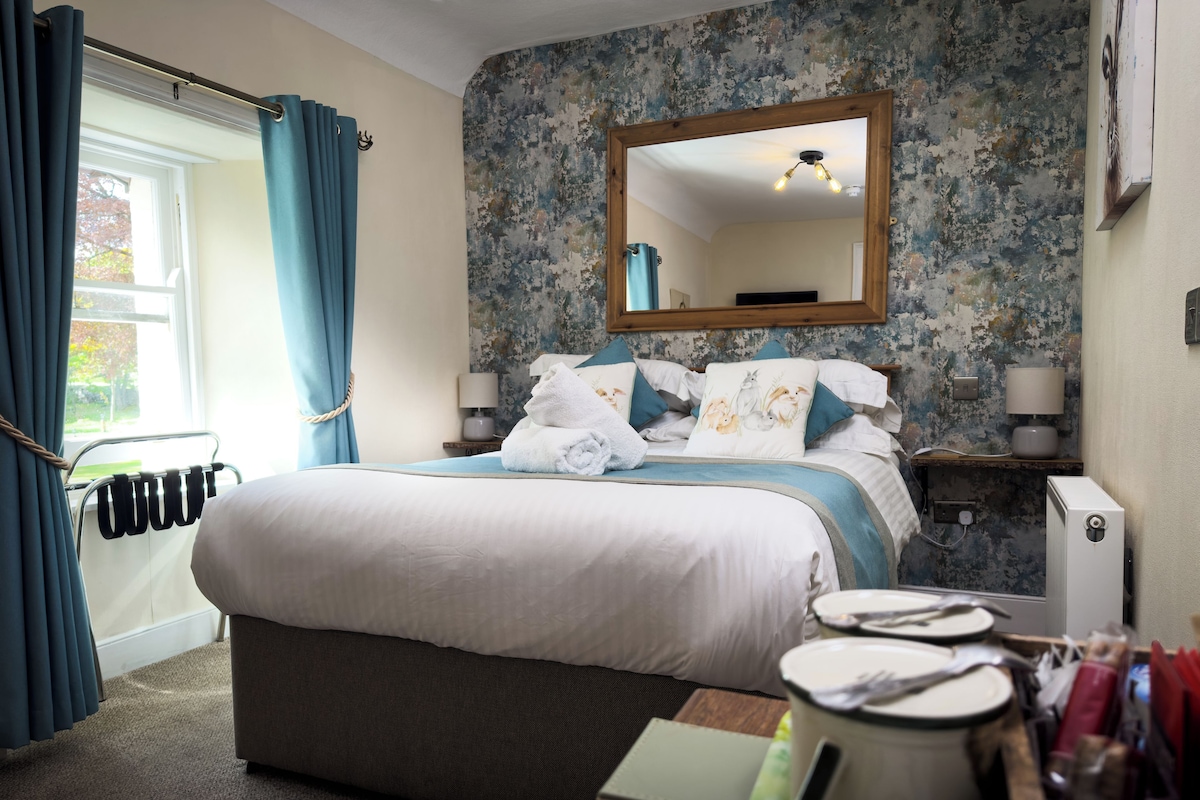 A hotel room with a large bed, a bedside table with a lamp, a mirror, and a view of the outdoors.
