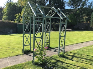 A green metal structure with a triangular roof, surrounded by a well-maintained lawn and a stone wall in the background.