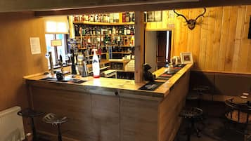 A bar area with a wooden counter, stools, and a variety of liquor bottles.