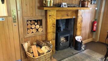 Interior de madera con chimenea, espacio para leña y una tetera de metal en un estante.