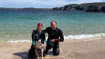 Two people on a beach with a dog, near the water.