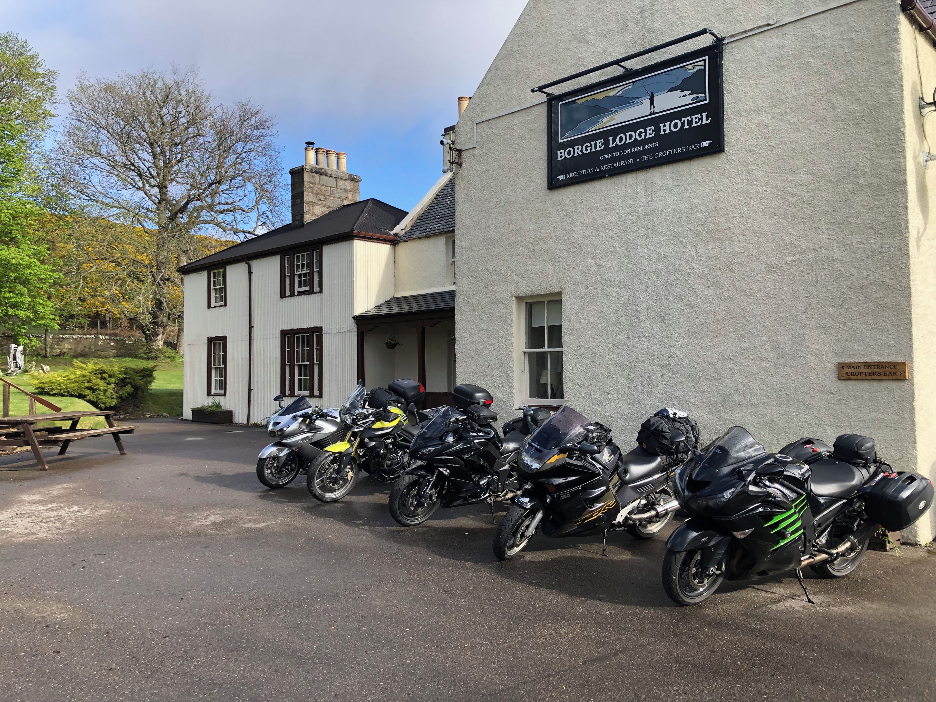 A row of motorcycles parked in front of a building with a sign that reads 'Borgie Lodge Hotel.'